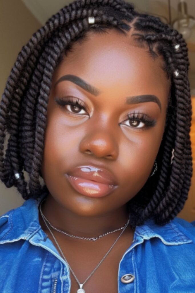 African American woman, plus size with chin-length crochet twist braids in a bob style, wearing denim top, taking selfie, brown eyes, full lips, dimples, silver necklace and earrings, big brown eyes with long lashes, soft glam makeup, full lips, wearing blue jean top and silver necklace.