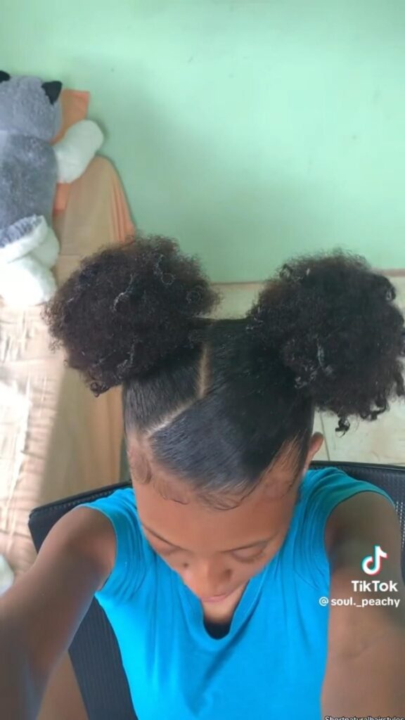Black girl taking an overhead selfie of her side part space buns.